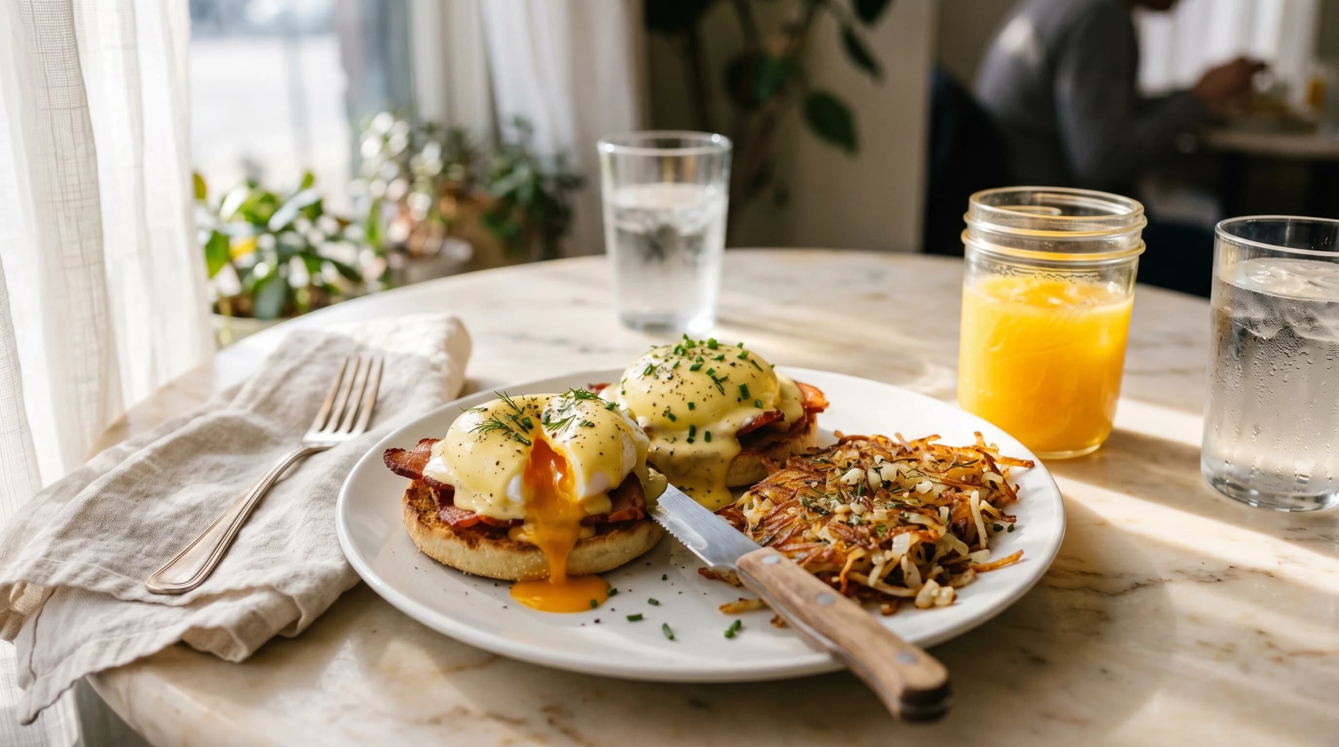 Brunch table with eggs benedict and fresh orange juice.